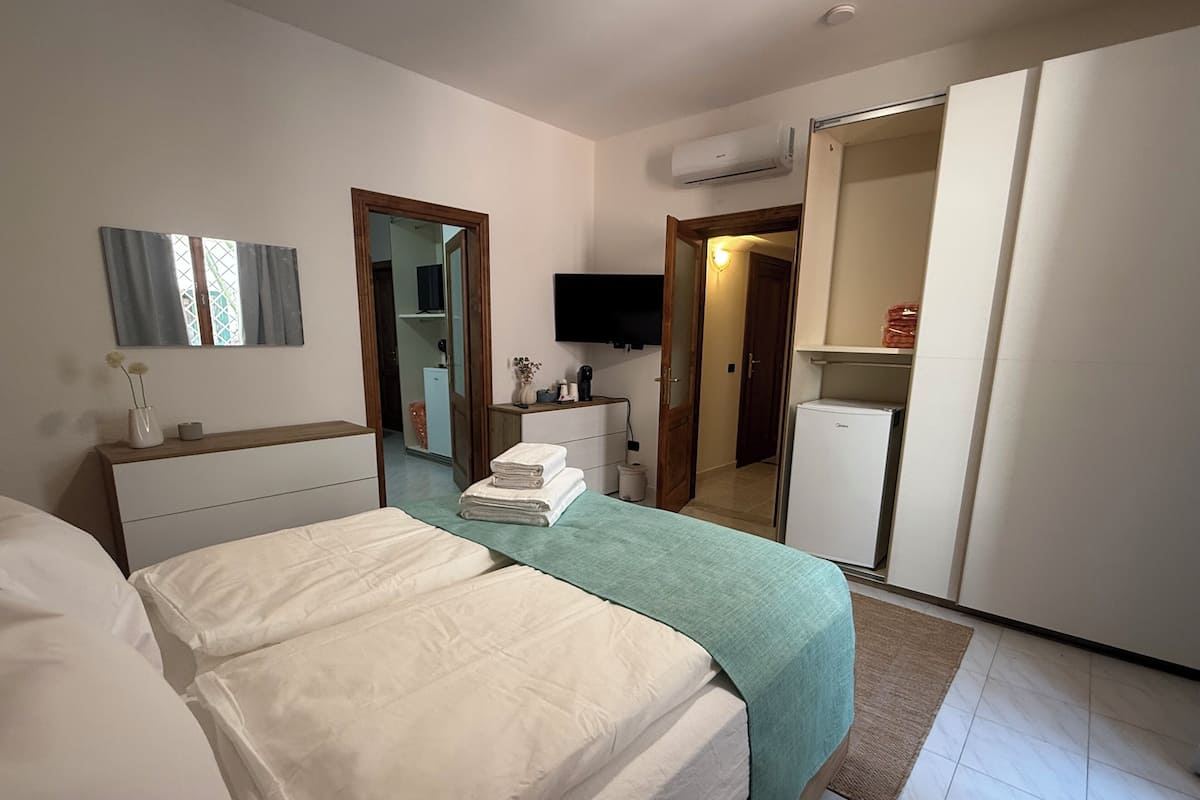 A bedroom with a bed, a TV, a wardrobe, and a small refrigerator.