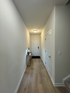 Un pasillo estrecho con suelo de madera, paredes blancas y una puerta al final.
