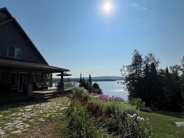A house with a patio overlooking a lake, surrounded by greenery and flowers.