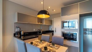 Uma cozinha moderna com eletrodomésticos embutidos, um espaço de jantar com mesa posta para dois e uma luminária pendente grande.