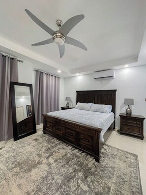 A bedroom with a bed, a ceiling fan, an air conditioning unit, a large mirror, two bedside tables with lamps, and a patterned rug. - Cozy view of the Harbour (Kingston)