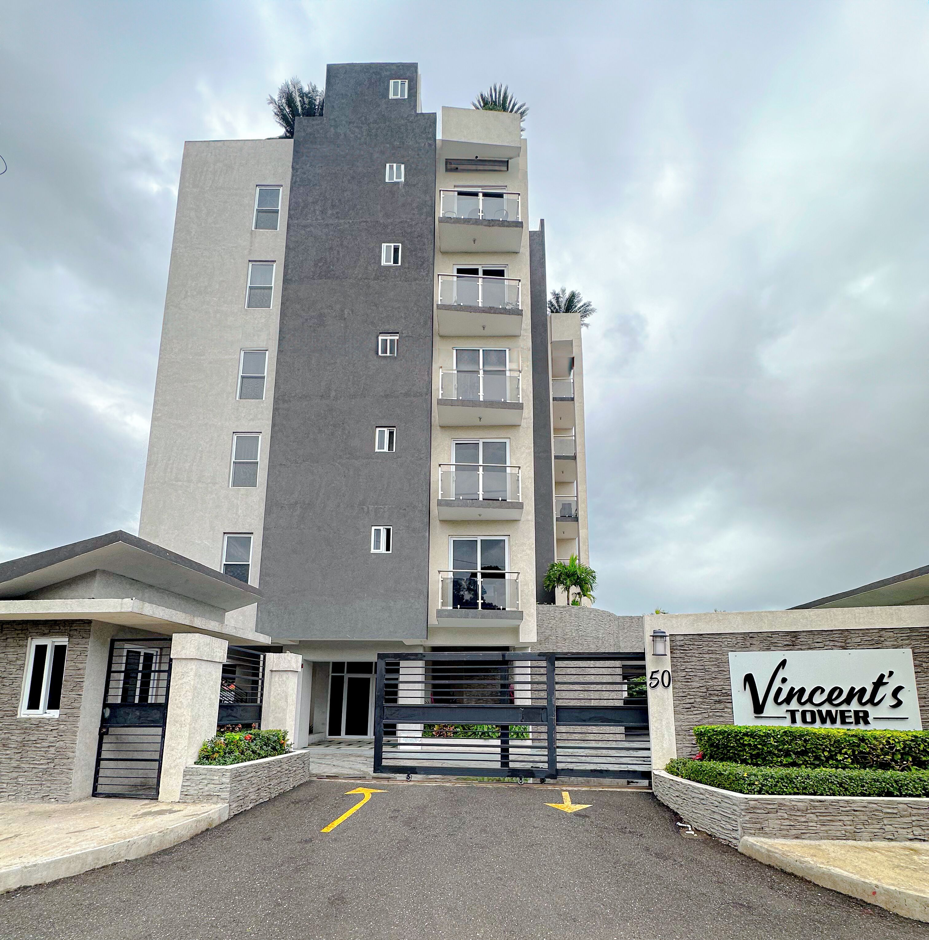 A multi-story building with a gated entrance, a sign reading 'Vincent's Tower,' and a clear sky.