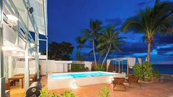 Zona de piscina exterior moderna con vista al océano y palmeras al anochecer.