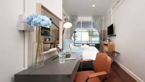 A hotel room with a bed, desk, chair, TV, and a view of the ocean. - Wander at Bayside 19 | Upstairs Sea-View King Room (sleeps up to 4) (Hua Hin)