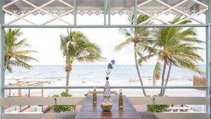 A wooden deck with a table and benches, overlooking a beach with palm trees and a pool. - Wander at Bayside 19 | Upstairs Sea-View King Room (sleeps up to 4) (Hua Hin)