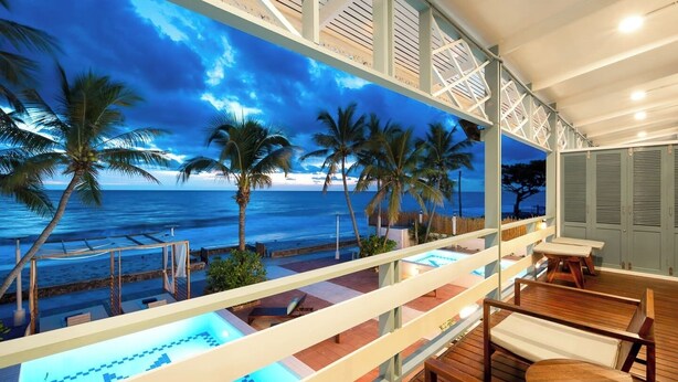 A balcony with a pool, palm trees, and a view of the ocean at dusk. - Wander at Bayside 19 | Upstairs Sea-View King Room (sleeps up to 4) (Hua Hin)