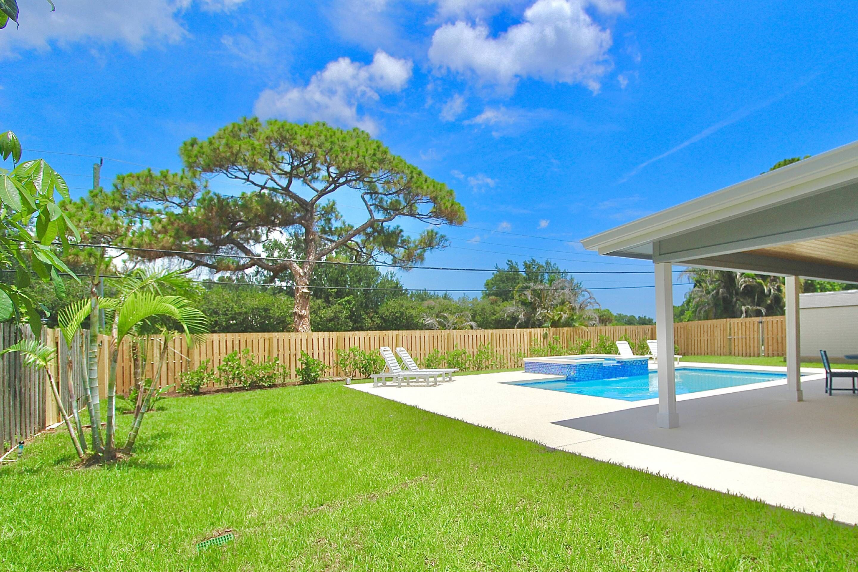 A backyard with a swimming pool, a wooden fence, and a large tree.