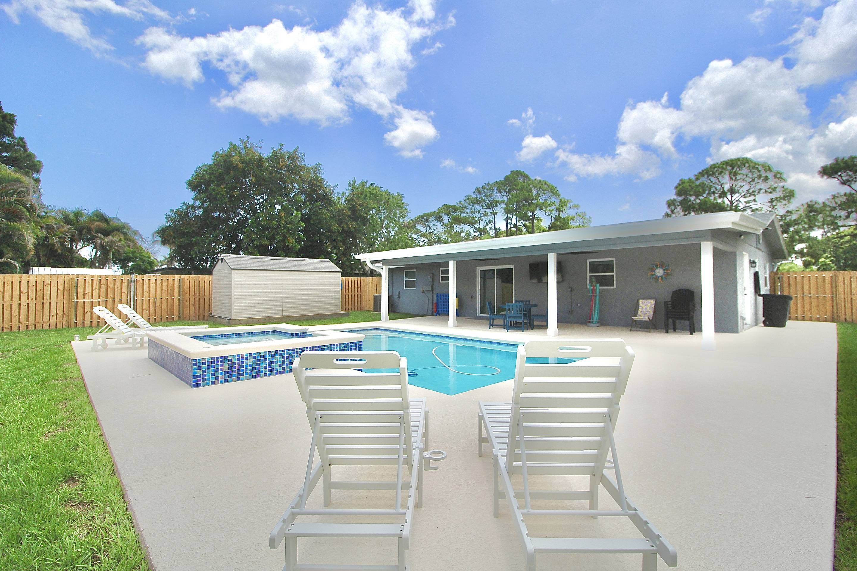 Ein Garten mit Swimmingpool, zwei Liegest ühlen und einer überdachten Terrasse.