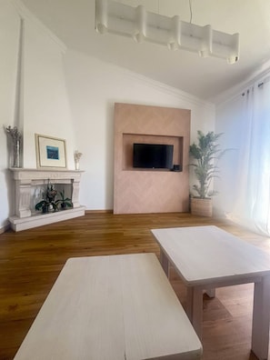 Ein Wohnzimmer mit Kamin, einem an der Wand befestigten Fernseher und zwei weißen Tischen.