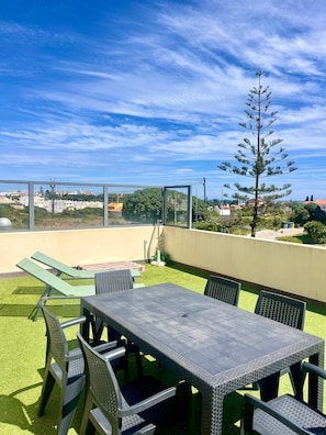 Eine Terrasse im Freien mit Tisch und Stühlen, eine grüne Rasenfläche und Blick auf die Umgebung.