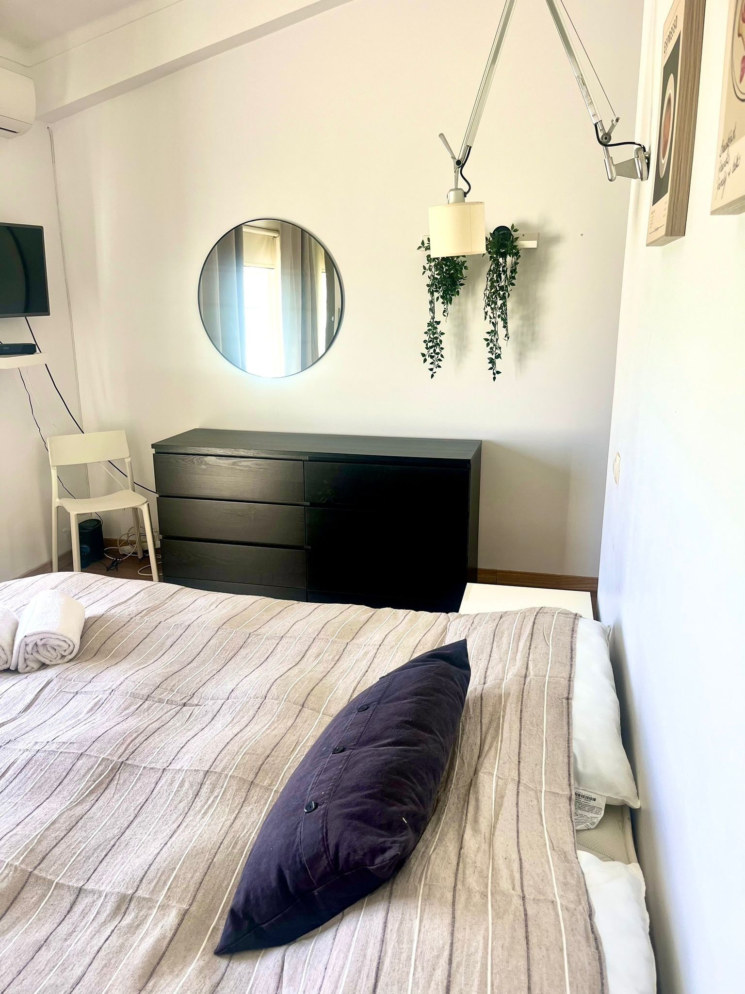 Une chambre à coucher avec un lit, une commode, un miroir et une plante suspendue.