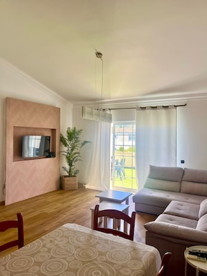 Ein Wohnzimmer mit Fernseher, Sofa und Essbereich mit Tisch und Stühlen.