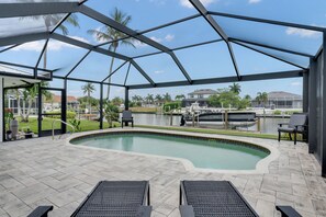 A covered outdoor swimming pool with lounge chairs, a view of a marina, and a clear sky. - Shell Yeah! Waterfront House with Private Pool in Palm Acres (Fort Myers)