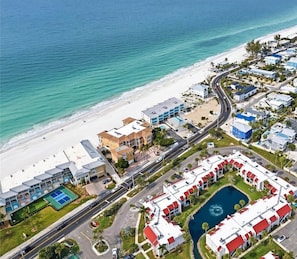 Luftaufnahme eines Küstenresorts mit Strandhäusern, einer Straße und einem Schwimmbecken.