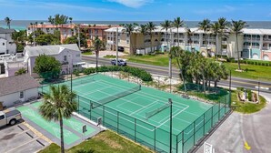 A tennis court surrounded by residential buildings, a parking area, and a road. - Island Breeze Escape (Bradenton Beach)