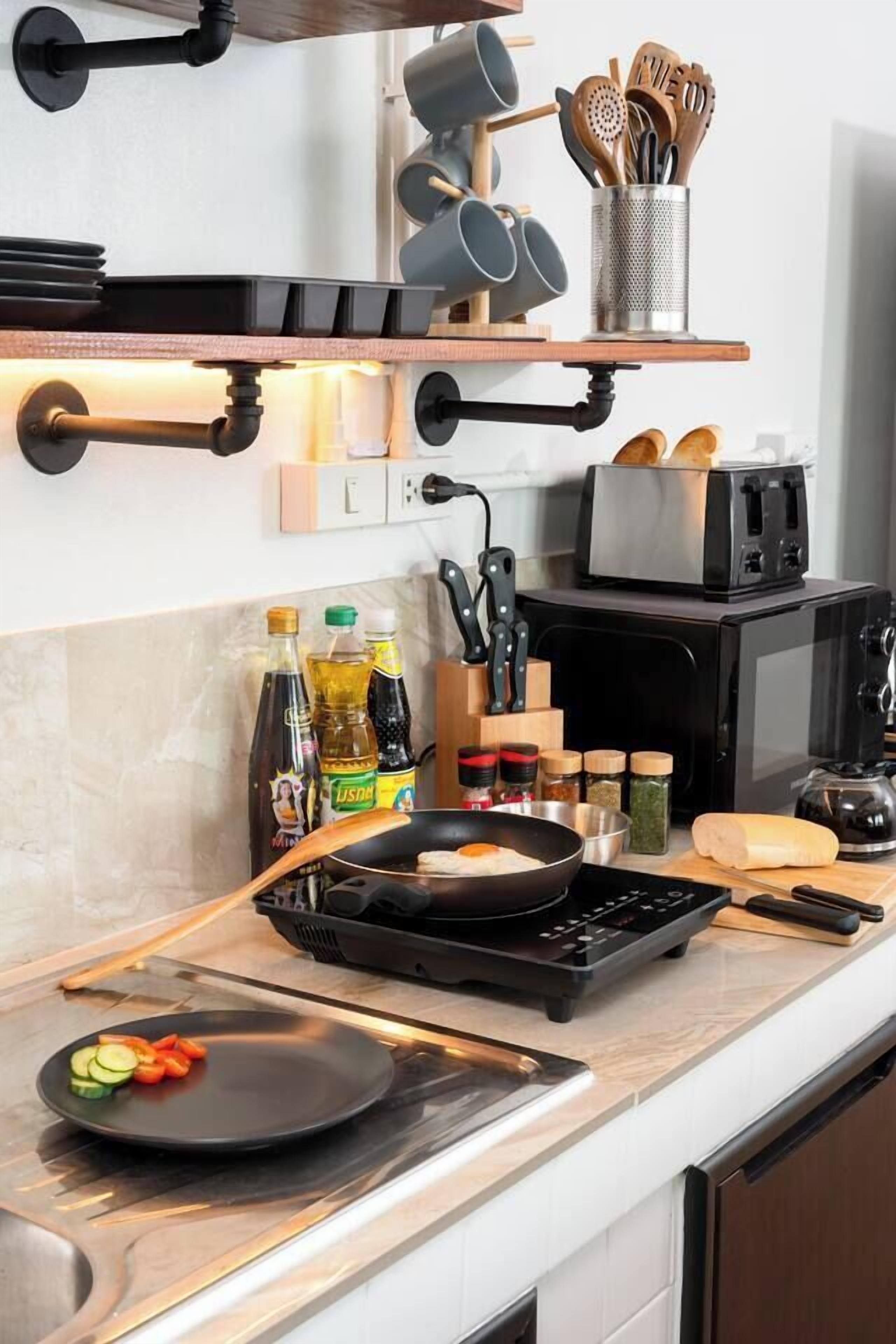 Una cocina moderna con una estufa negra, un tostador y varios utensilios de cocina en estantes.