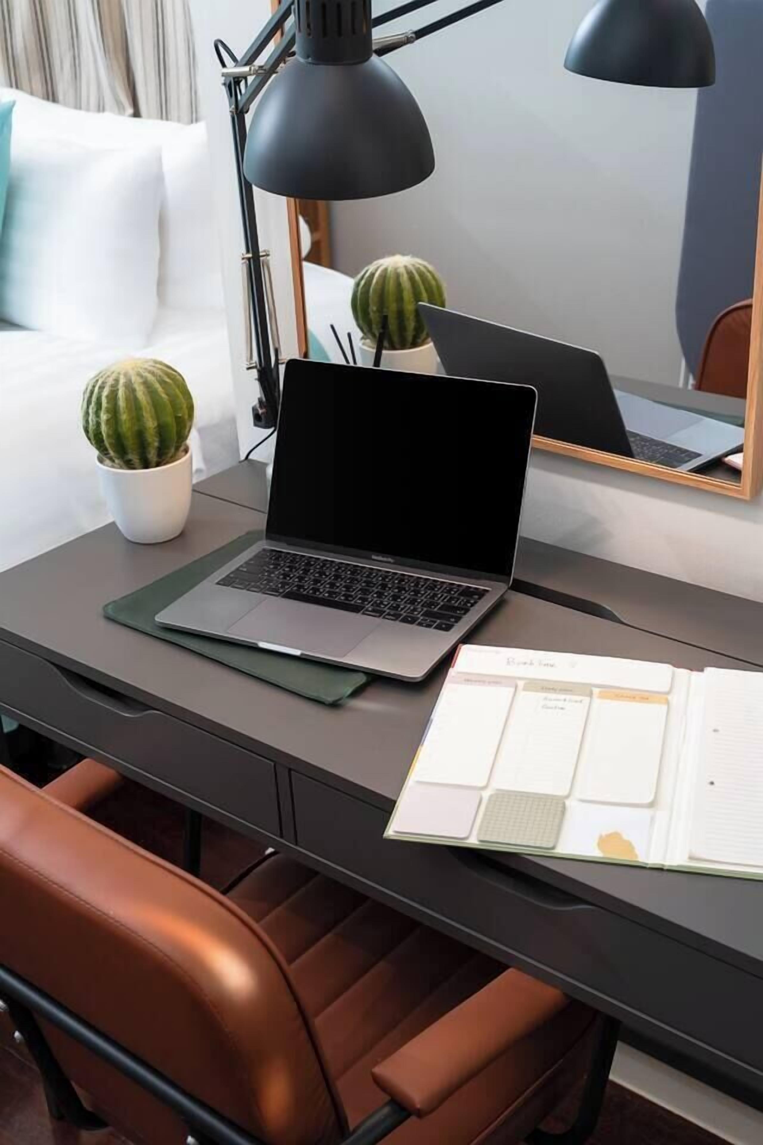 En bærbar computer på et skrivebord med en lampe, to krukkeplanter og en notesbog.