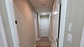 Un couloir étroit avec un plancher en bois, des portes blanches et un luminaire au plafond.