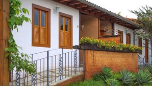 A two-story house with a balcony, a stone pathway, and a brick wall with yellow flowers.