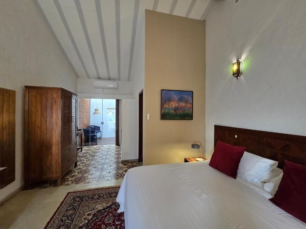 Un cuarto de hotel con cama, mesita de noche, lámpara, un cuadro en la pared y un armario de madera.