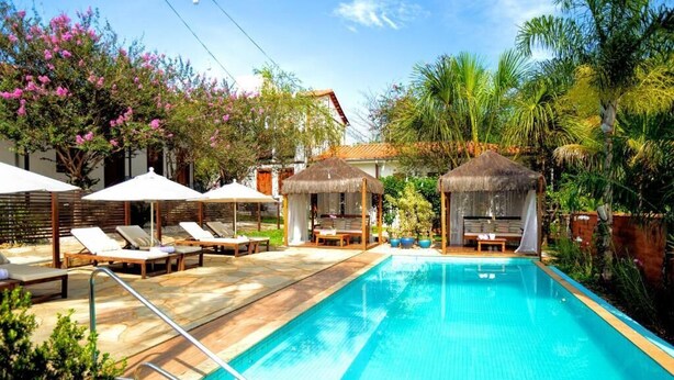 Une piscine entourée de plantes tropicales et agrémentée de chaises longues et de parasols, avec une structure à toit de chaume.