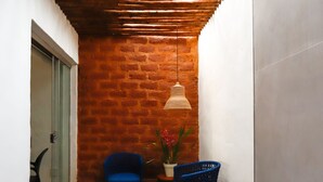 Une salle de bain moderne avec une baignoire blanche, une chaise bleue, une lampe en osier et un mur en briques.