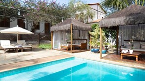A swimming pool with lounge chairs and thatched-roof cabanas.