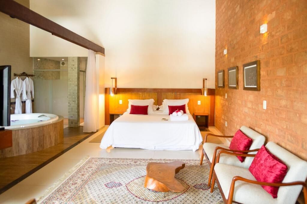 A hotel room with a large bed, a sitting area with chairs, a wooden coffee table, a bathtub, and a shower area.