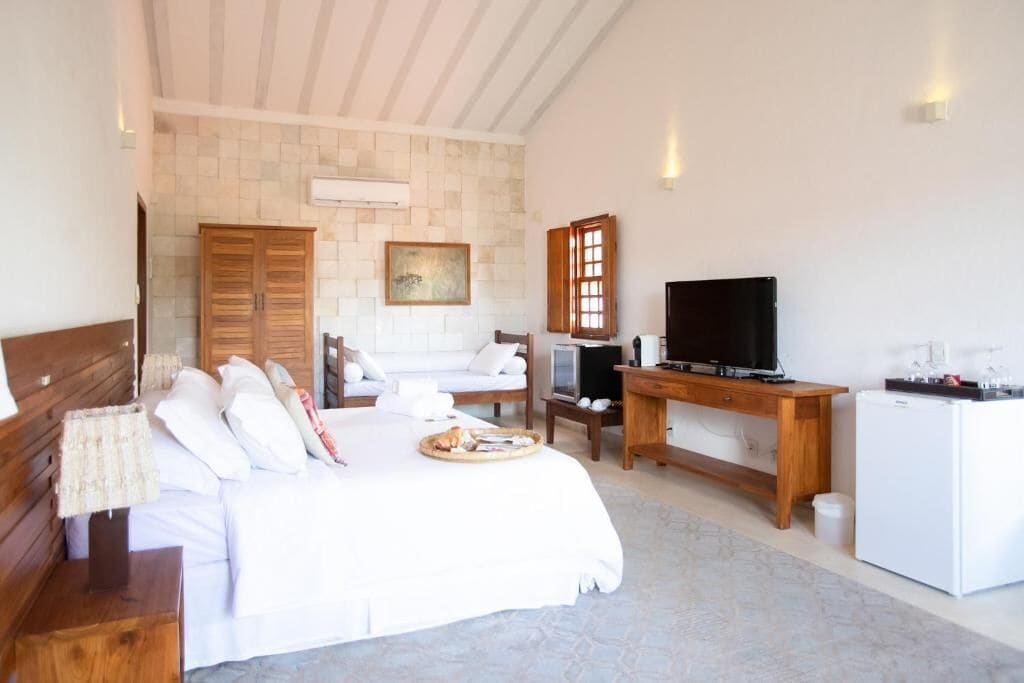 A bedroom with a bed, a TV, a desk, a wardrobe, and a small fridge.