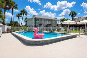 Ein Swimmingpool mit einem rosa Flamingo-Schwimmpfaugel, umgeben von einem weißen Zaun, Palmen und einem Gebäude mit einer Treppe.