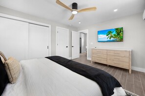 Ein Schlafzimmer mit einem Bett, einem Deckenventilator, einem Schminktisch und einem Bild einer tropischen Szene.