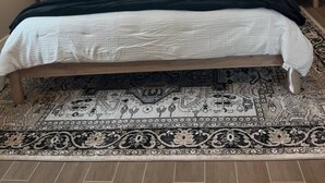 Ein Schlafzimmer mit einem Bett, zwei Nachttischen mit Lampen, einem Deckenventilator, einem Fenster und einem gemusterten Teppich.