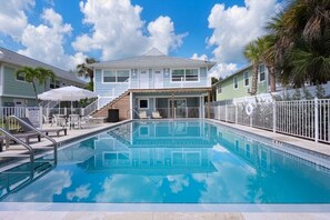 A swimming pool with a clear blue sky and clouds in the background, surrounded by a white fence and palm trees. - The Wells at Coconut Cove (Fort Myers Beach)