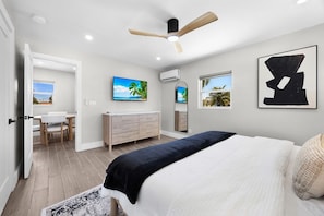 Ein Schlafzimmer mit Bett, Deckenventilator, Fernseher, Kommode und Fenster mit Blick.