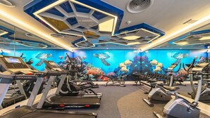 Una palestra con tapis roulant, macchinari ellittici e un murale con creature marine.
