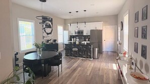 Una cocina moderna con una isla central, un comedor con mesa redonda y un espacio amplio y luminoso con piso de madera.