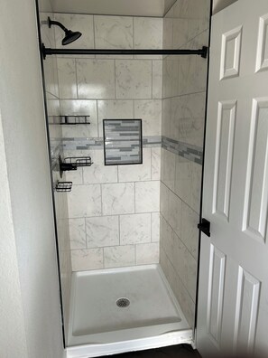 Eine begehbare Dusche mit Glastür, weißen Marmorfliesen, einer Duschbrause und einem gerahmten Bild an der Wand.