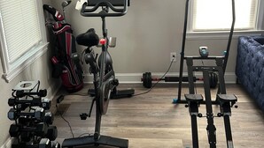 Un gimnasio en casa con equipo de ejercicio, un televisor y una estanter ía con objetos decorativos.