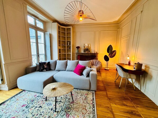 A living room with a sofa, a small table, a floor lamp, and a bookshelf. - Le Bovary - Charming studio on the château side (Vendôme)