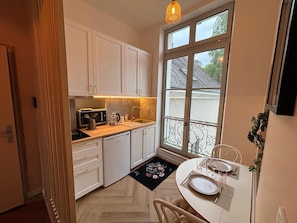 A compact kitchen with white cabinets, a countertop microwave, and a dining area with a table set for two. - Le Bovary - Charming studio on the château side (Vendôme)