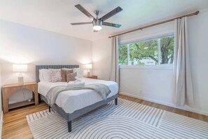 A bedroom with a bed, bedside tables, a ceiling fan, a window with curtains, and a view of trees outside. - 4BR Home w/ Hot Tub, Grill, Foosball & Cornhole (Reno)