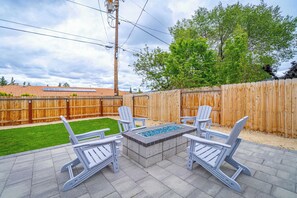 An outdoor patio with Adirondack chairs, a rectangular fire pit, and a wooden fence. - 4BR Home w/ Hot Tub, Grill, Foosball & Cornhole (Reno)