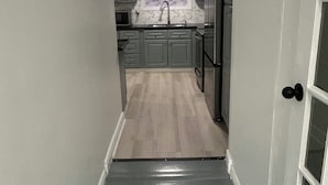 Un pasillo estrecho que conduce a una cocina con armarios grises, un lavabo y un refrigerador.