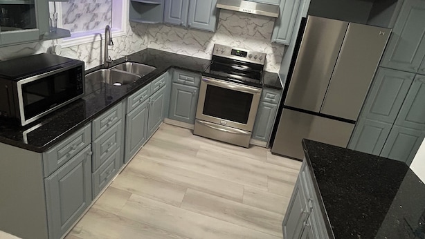 Una cocina moderna con armarios grises, un refrigerador de acero inoxidable, un horno empotrado y un microondas.