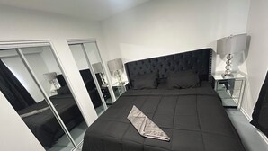 Un dormitorio con una cama grande, un espejo, una mesita de noche con lámpara y un armario.