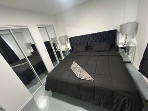 Une chambre à coucher avec un grand lit, un miroir, une table de chevet avec une lampe et une armoire.