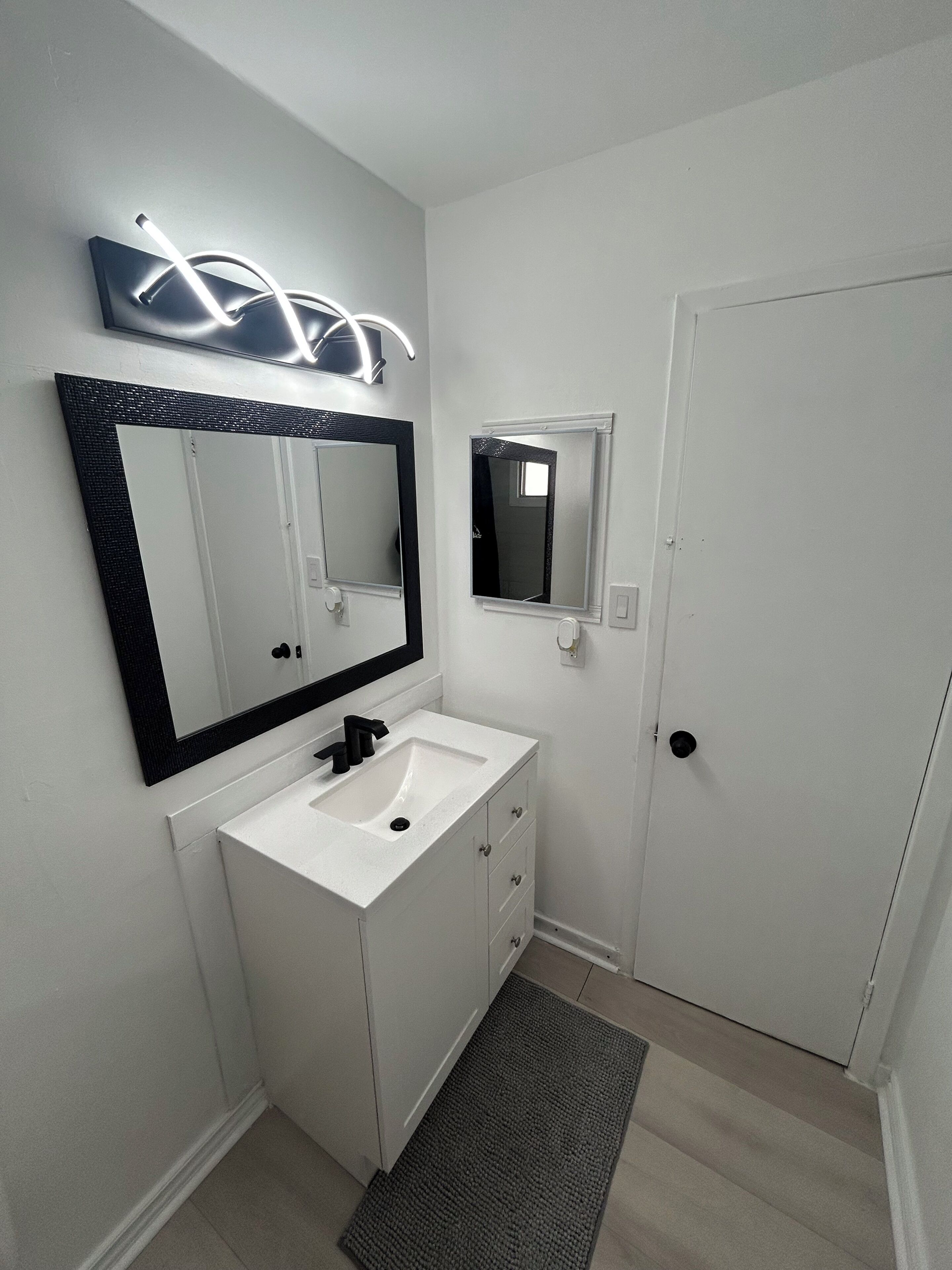 Een badkamer met een witte wastafel, een grote spiegel en een kleine spiegel.