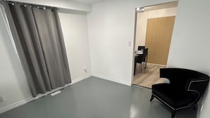 Una habitación amplia con suelo gris, una silla negra y una puerta que da a otra zona con una mesa y sillas.