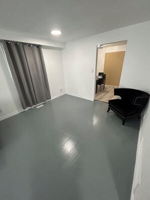 Une pièce spacieuse avec un sol gris, une chaise noire et une porte donnant sur un autre espace comprenant une table et des chaises.