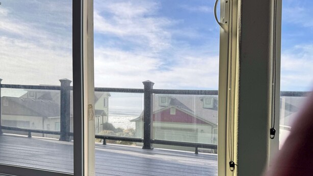En vy genom ett fönster med en träveranda, ett metallräcke och en dörrmatta.